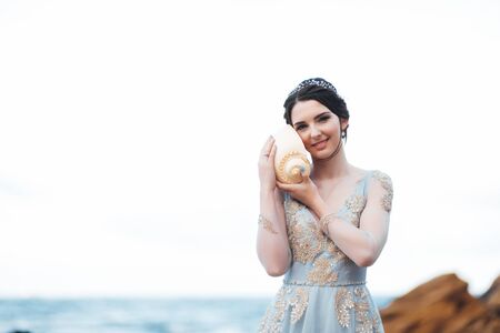 bride with a big shell on the beach in a blue wedding dressの写真素材