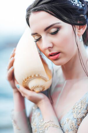 bride with a big shell on the beach in a blue wedding dressの写真素材