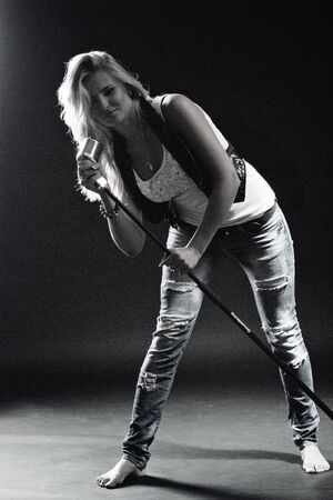 young, girl, blonde, jeans, clothes on a dark background emotionally sings into a microphoneの写真素材