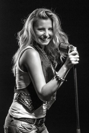 young, girl, blonde, jeans, clothes on a dark background emotionally sings into a microphoneの写真素材