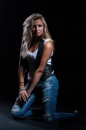 young, girl, blonde, jeans, clothes on a dark background kneelsの写真素材