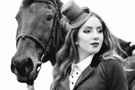 red-haired jockey girl in a red cardigan and black high boots with a horse for a walkの写真素材