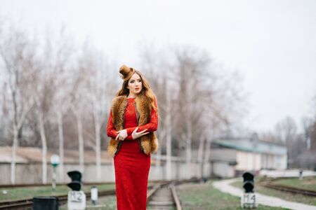 young girl with red hair in a bright red dress on the railway tracks of the stationの写真素材