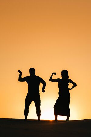 silhouettes of a happy young couple guy and girl on a background of orange sunset in the sand desertの写真素材