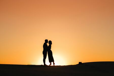 silhouettes of a happy young couple guy and girl on a background of orange sunset in the sand desertの写真素材