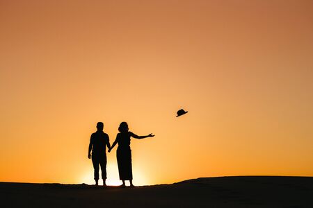 silhouettes of a happy young couple guy and girl on a background of orange sunset in the sand desertの写真素材