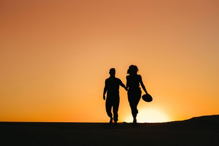 silhouettes of a happy young couple guy and girl on a background of orange sunset in the sand desertの写真素材