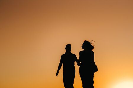 silhouettes of a happy young couple guy and girl on a background of orange sunset in the sand desertの写真素材