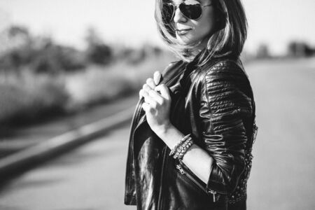 red-haired girl in a black jacket and blue glasses on a gray roadの写真素材