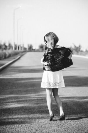 red-haired girl in a black jacket and blue glasses on a gray roadの写真素材