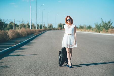 red-haired girl in a black jacket and blue glasses on a gray roadの写真素材