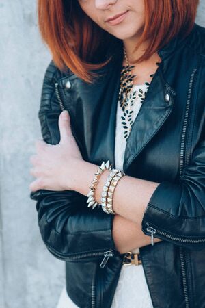 red-haired girl in a black jacket and blue glasses on a gray roadの写真素材