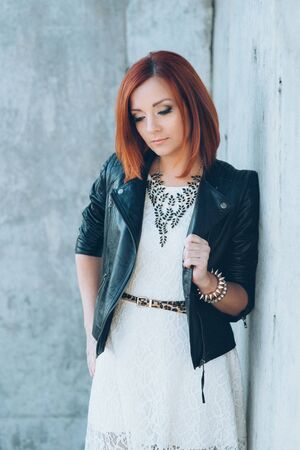 red-haired girl in a black jacket and blue glasses on a gray roadの写真素材