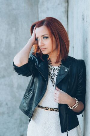 red-haired girl in a black jacket and blue glasses on a gray roadの写真素材