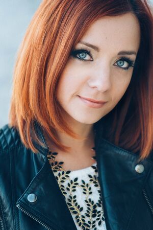 red-haired girl in a black jacket and blue glasses on a gray roadの写真素材