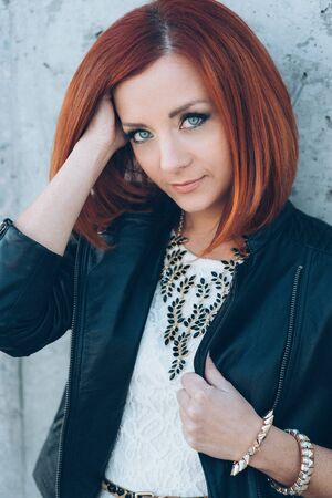 red-haired girl in a black jacket and blue glasses on a gray roadの写真素材