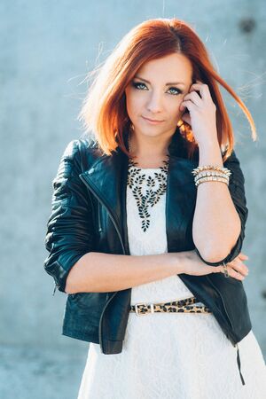 red-haired girl in a black jacket and blue glasses on a gray roadの写真素材