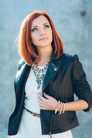 red-haired girl in a black jacket and blue glasses on a gray roadの写真素材