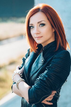 red-haired girl in a black jacket and blue glasses on a gray roadの写真素材
