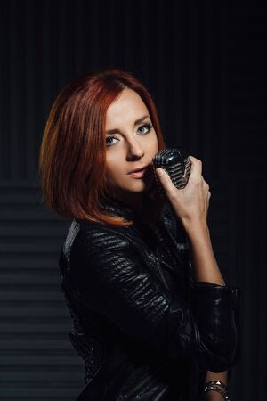 young red-haired girl in a white dress and a black leather rocker jacket sings emotionally into the microphoneの写真素材