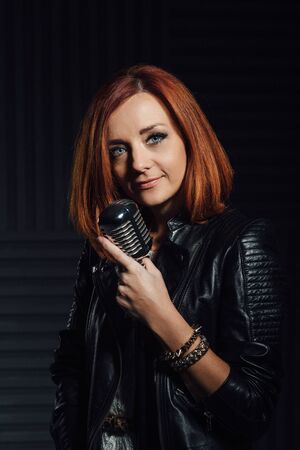 young red-haired girl in a white dress and a black leather rocker jacket sings emotionally into the microphoneの写真素材