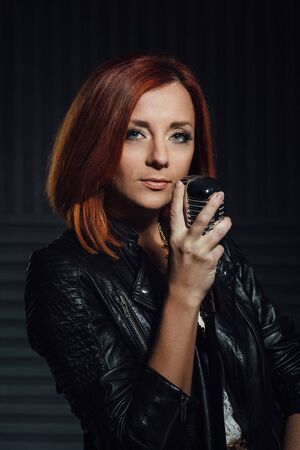 young red-haired girl in a white dress and a black leather rocker jacket sings emotionally into the microphoneの写真素材