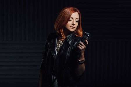 young red-haired girl in a white dress and a black leather rocker jacket sings emotionally into the microphoneの写真素材
