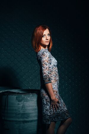 redheaded model girl in a long dress in a dark industrial Studio near barrels of oilの写真素材