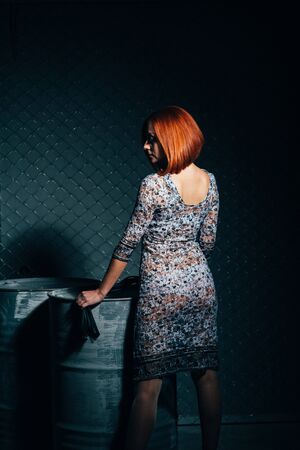redheaded model girl in a long dress in a dark industrial Studio near barrels of oilの写真素材