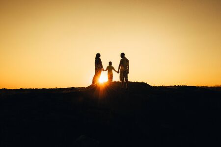 silhouettes of a happy young happy family against an orange sunset in the desertの写真素材