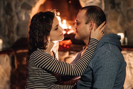 guy and girl are sitting in a wooden house on the background of a burning fireplaceの写真素材