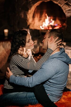 guy and girl are sitting in a wooden house on the background of a burning fireplaceの写真素材