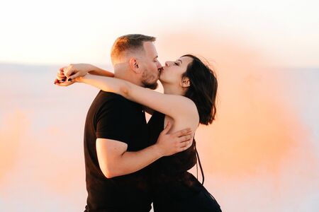 guy and a girl in black clothes hug and run on the white sand with orange smokeの写真素材