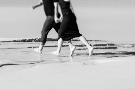 young couple a guy with a girl in black clothes are walking on the white sand at the edge of blue waterの写真素材