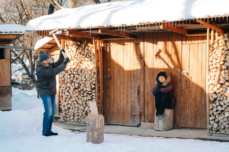 guy in winter clothes chopping wood in the yard, covered with snowの写真素材