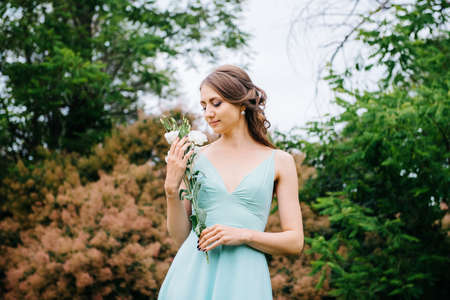 Happy girl in a turquoise long dress in a green park on a background of herbs, trees and rose bushesの写真素材