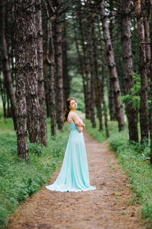 Happy girl in a turquoise long dress in a green park on a background of herbs, trees and rose bushesの写真素材