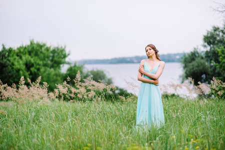 Happy girl in a turquoise long dress in a green park on a background of herbs, trees and rose bushesの写真素材