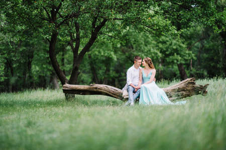 happy guy in a white shirt and a girl in a turquoise dress, the bride and groom are walking in the forest parkの写真素材
