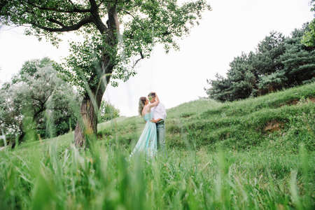 happy guy in a white shirt and a girl in a turquoise dress, the bride and groom are walking in the forest parkの写真素材