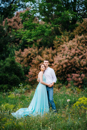 happy guy in a white shirt and a girl in a turquoise dress, the bride and groom are walking in the forest parkの写真素材