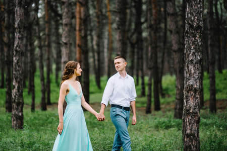 happy guy in a white shirt and a girl in a turquoise dress, the bride and groom are walking in the forest parkの写真素材