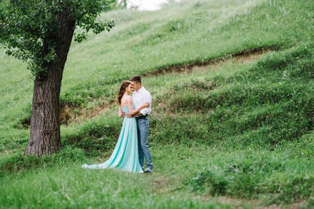 happy guy in a white shirt and a girl in a turquoise dress, the bride and groom are walking in the forest parkの写真素材