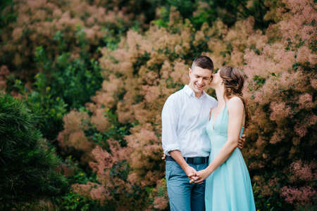 happy guy in a white shirt and a girl in a turquoise dress, the bride and groom are walking in the forest parkの写真素材