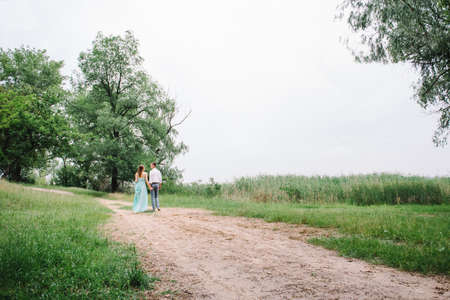 happy guy in a white shirt and a girl in a turquoise dress, the bride and groom are walking in the forest parkの写真素材