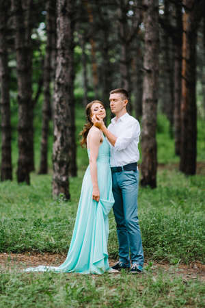 happy guy in a white shirt and a girl in a turquoise dress, the bride and groom are walking in the forest parkの写真素材