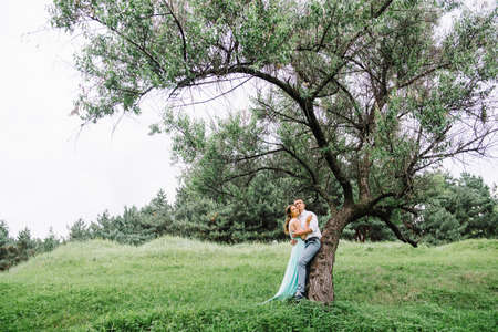 happy guy in a white shirt and a girl in a turquoise dress, the bride and groom are walking in the forest parkの写真素材