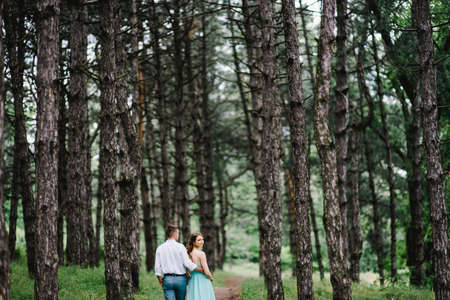 happy guy in a white shirt and a girl in a turquoise dress, the bride and groom are walking in the forest parkの写真素材