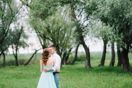 happy guy in a white shirt and a girl in a turquoise dress, the bride and groom are walking in the forest parkの写真素材