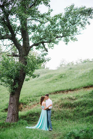 happy guy in a white shirt and a girl in a turquoise dress, the bride and groom are walking in the forest parkの写真素材